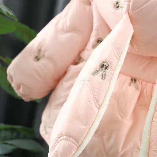 Close-up of a soft pink children's quilted jacket with brown embroidered ribbons and cozy design