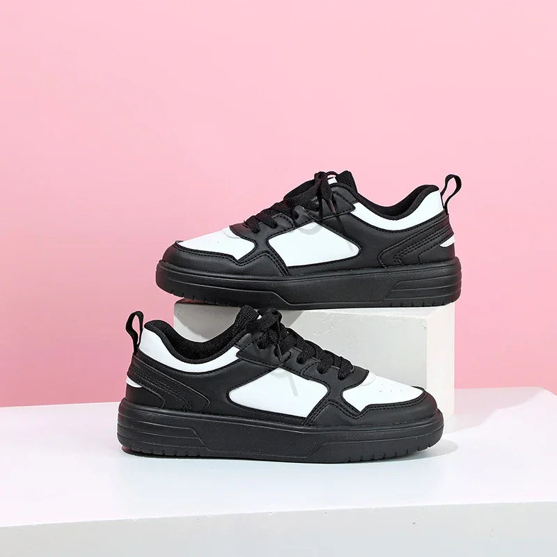 Pair of black and white low-top sneakers displayed on white geometric pedestals with pink background