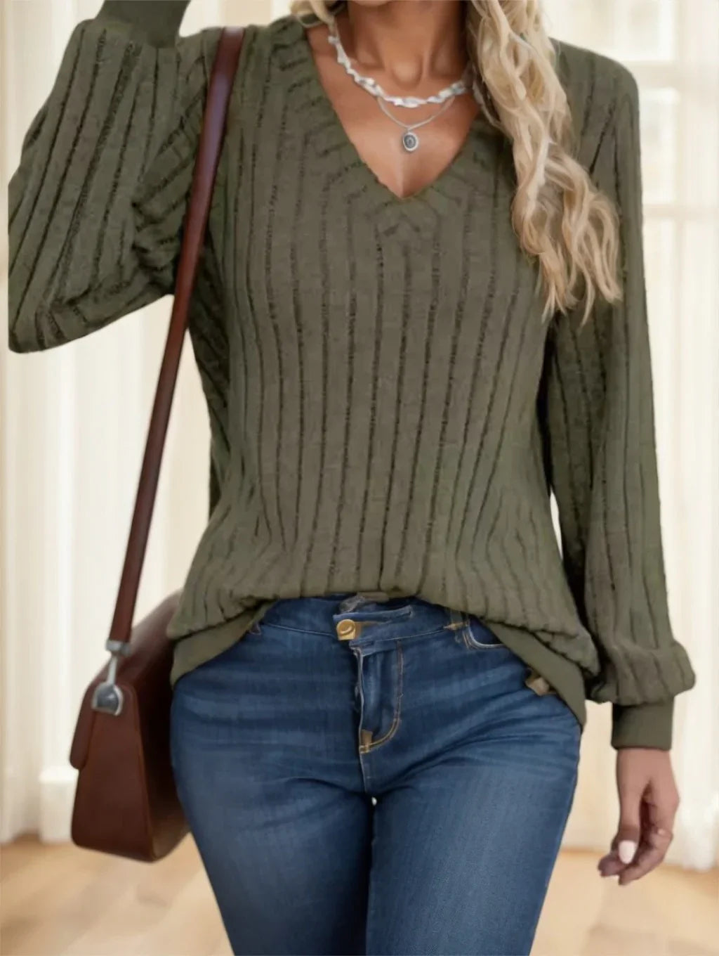 Woman wearing green ribbed V-neck sweater, blue jeans, silver necklaces, and carrying brown shoulder bag
