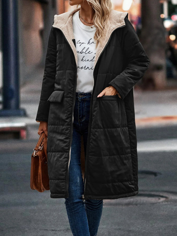 Woman wearing black long puffer coat with sherpa lining, blue jeans, and holding brown handbag on city street