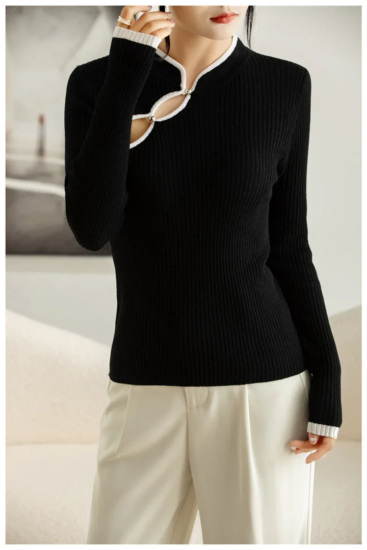 Woman wearing black ribbed knit sweater with white trim keyhole neckline and white pants indoors