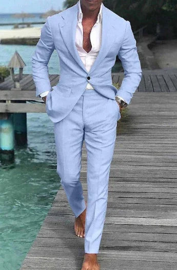 Man wearing light blue suit and unbuttoned white shirt walking barefoot on wooden dock by turquoise water