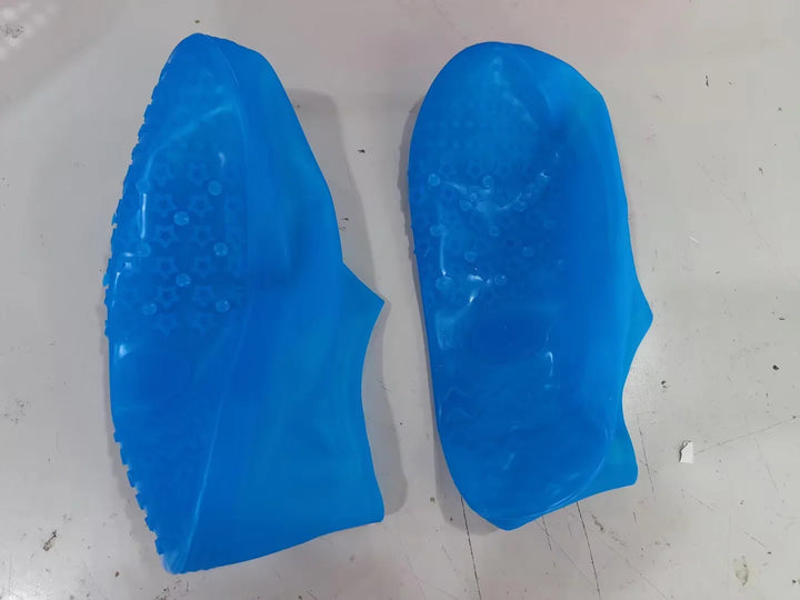 Pair of blue silicone shoe covers with textured sole for grip on a white surface