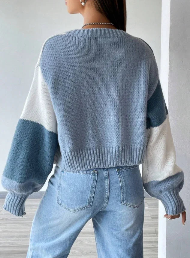 Back view of woman wearing a color block knitted sweater with blue, white, and gray sleeves paired with light blue denim jeans