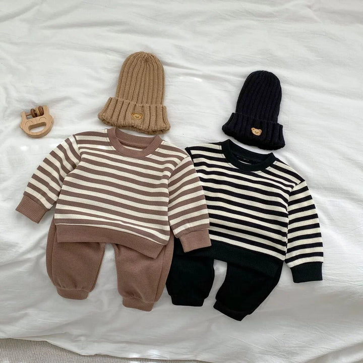 Two baby outfits with striped tops and matching pants, brown set with beanie and black set with beanie on white fabric
