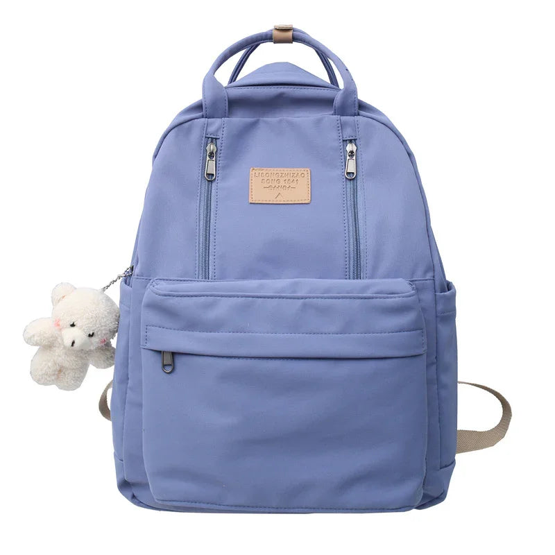 Light blue casual backpack with front pockets and a small white teddy bear keychain attached