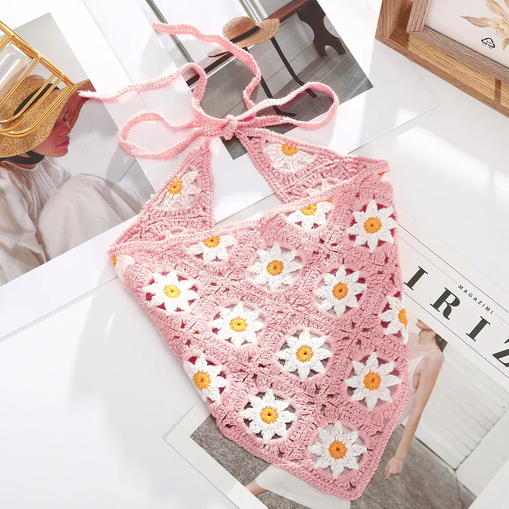 Pink crochet halter top with white and yellow daisy flower patterns on white surface with magazines