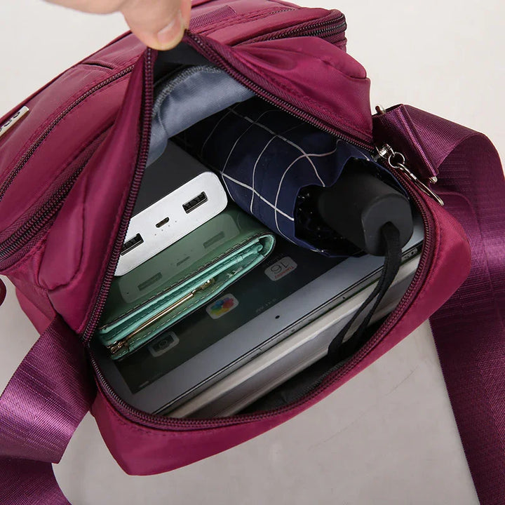 Open purple crossbody bag with portable charger, folded umbrella, green wallet, and tablet inside