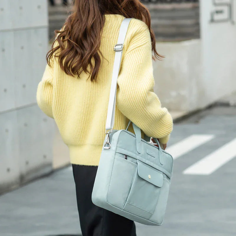 Woman wearing yellow sweater carrying light blue laptop bag with shoulder strap on city street