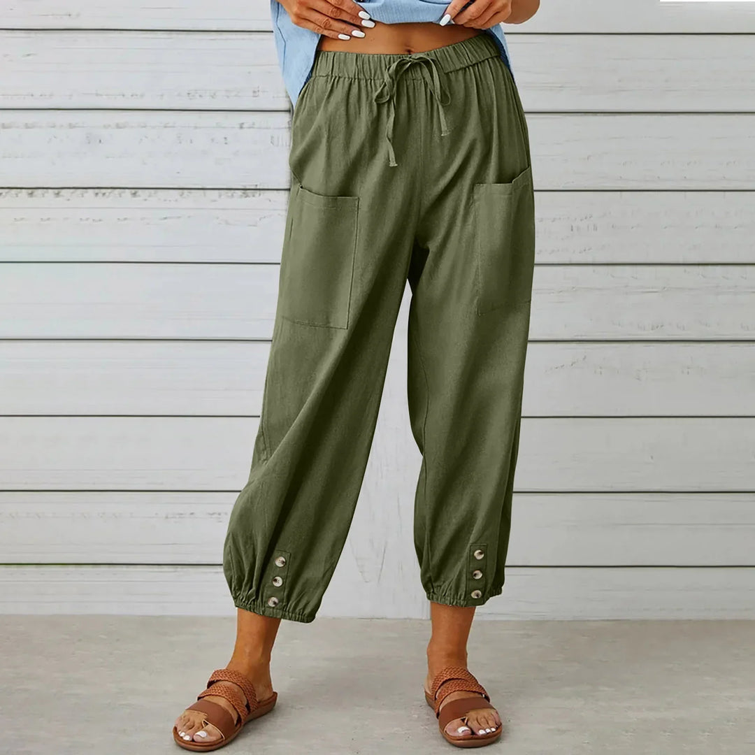 Woman wearing olive green drawstring pants with front pockets and buttoned cuffs, paired with brown sandals