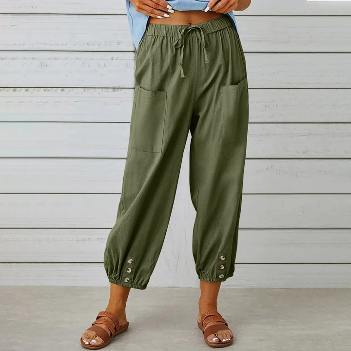 Woman wearing olive green drawstring pants with front pockets and buttoned cuffs, paired with brown sandals