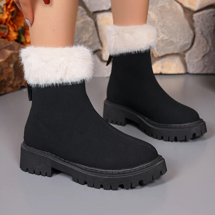 Black winter boots with thick chunky soles and white faux fur cuffs on gray floor