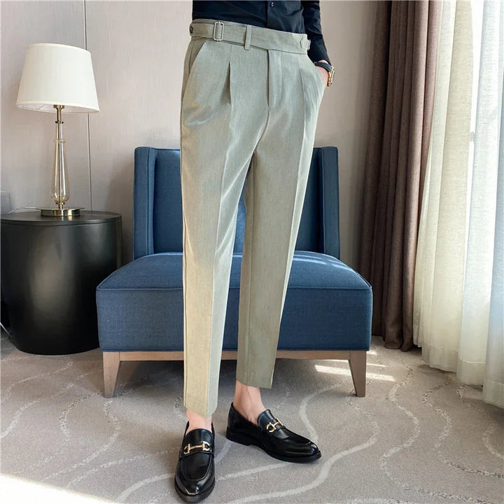 Person wearing beige tailored trousers with belt detail and black leather loafers in modern room