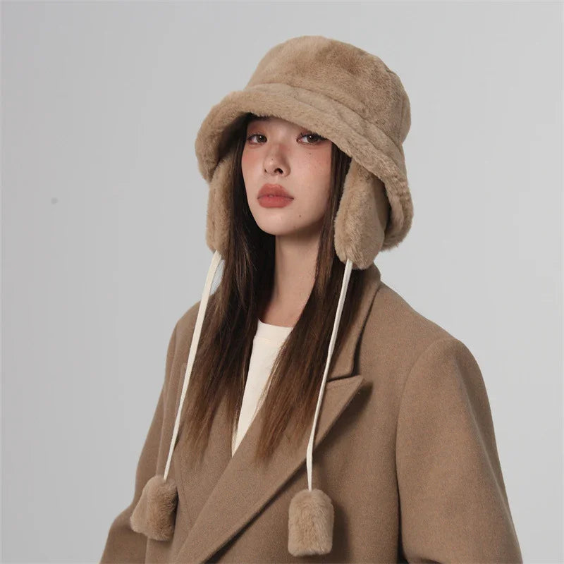 Woman wearing a beige faux fur trapper hat and matching beige wool coat against a gray background