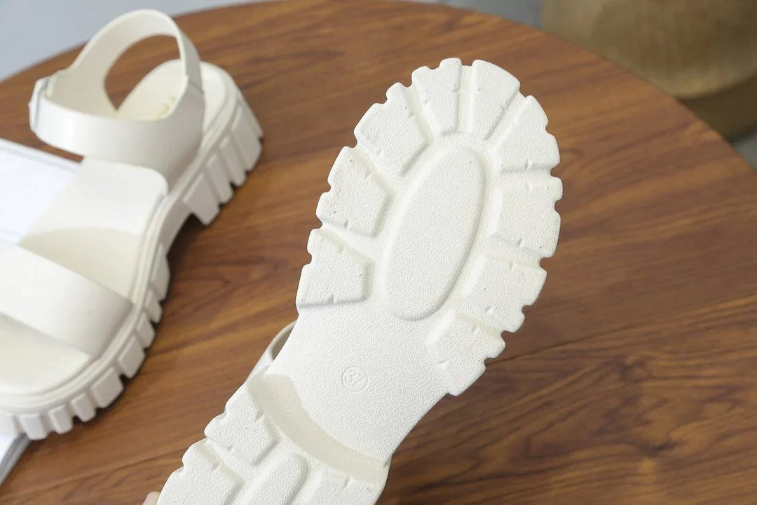 Close-up of white chunky sole sandals on wooden table, featuring thick straps and textured outsole