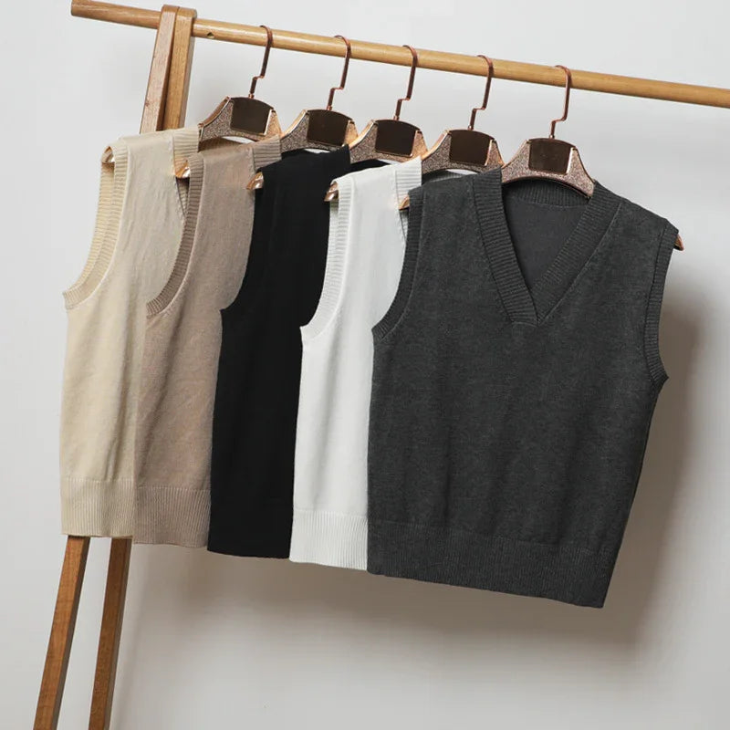 Five sleeveless V-neck knit sweater vests in beige, brown, black, white, and gray on wooden hangers