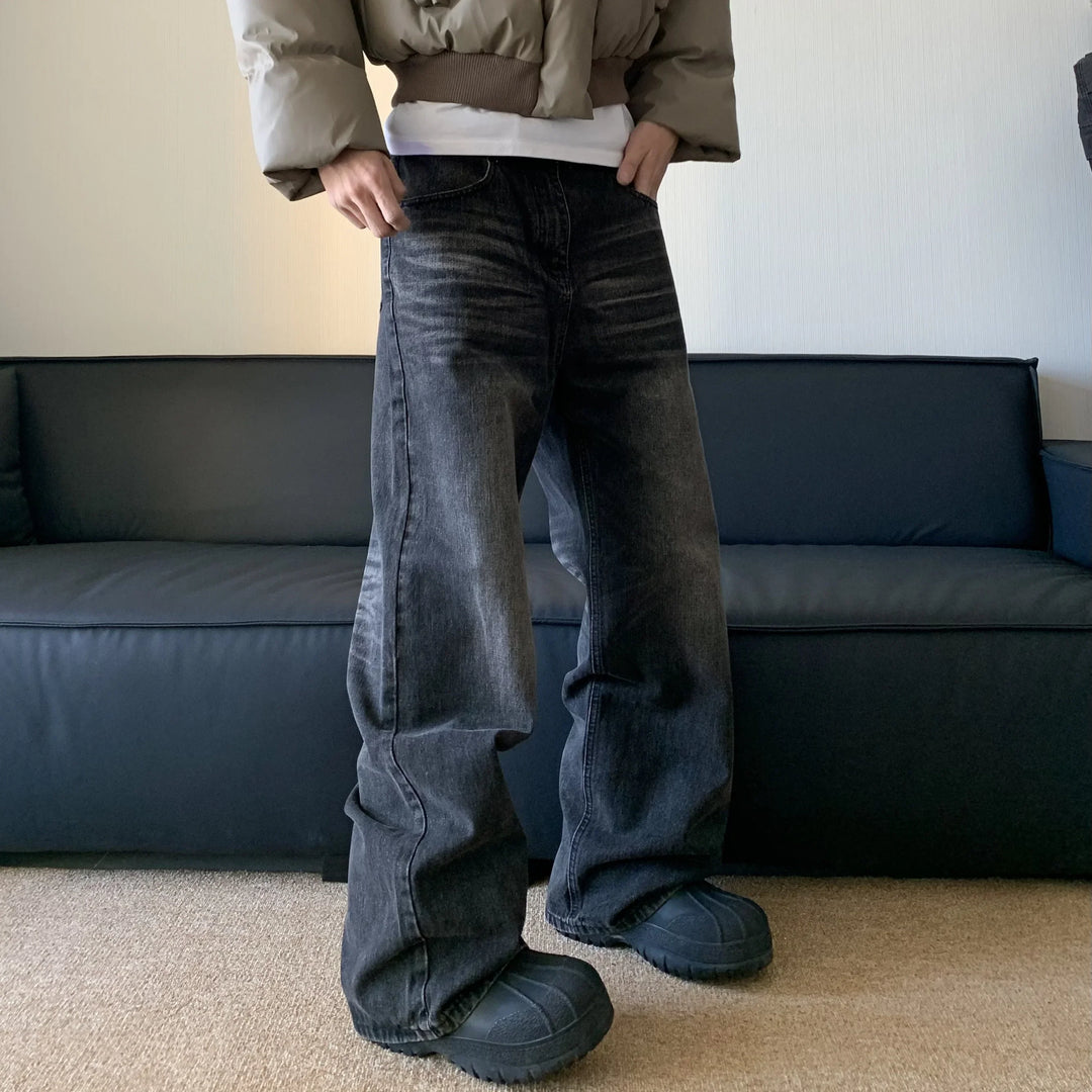 Person wearing black faded wide-leg jeans and black chunky shoes standing in front of dark gray sofa indoors