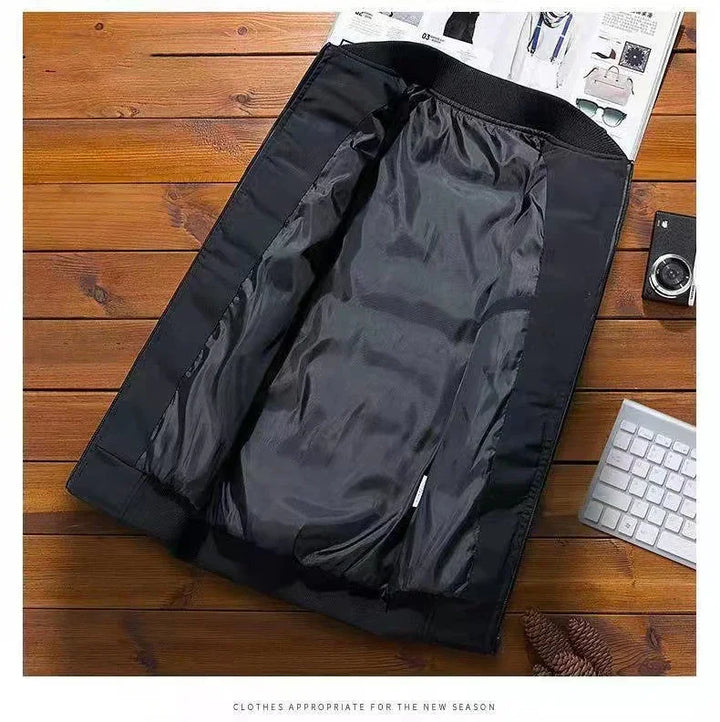 Black lightweight jacket laid open on wooden surface with keyboard, camera, and magazine