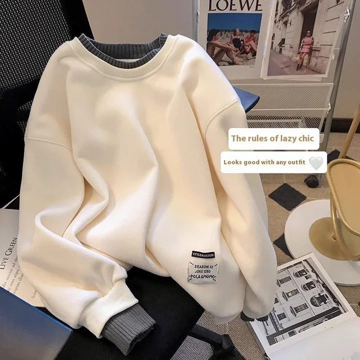 White crewneck sweatshirt with grey inner cuffs and label, laid on black chair in cozy room