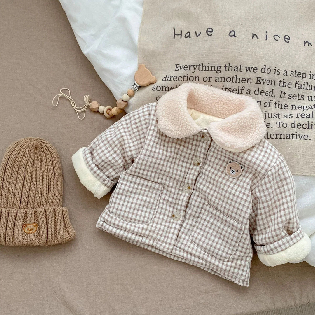 Baby plaid jacket with teddy bear patch and sherpa collar next to beige knit hat and wooden toy