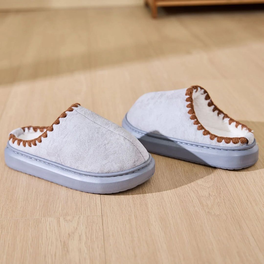 Light gray cozy indoor slippers with brown trim and soft lining on wooden floor