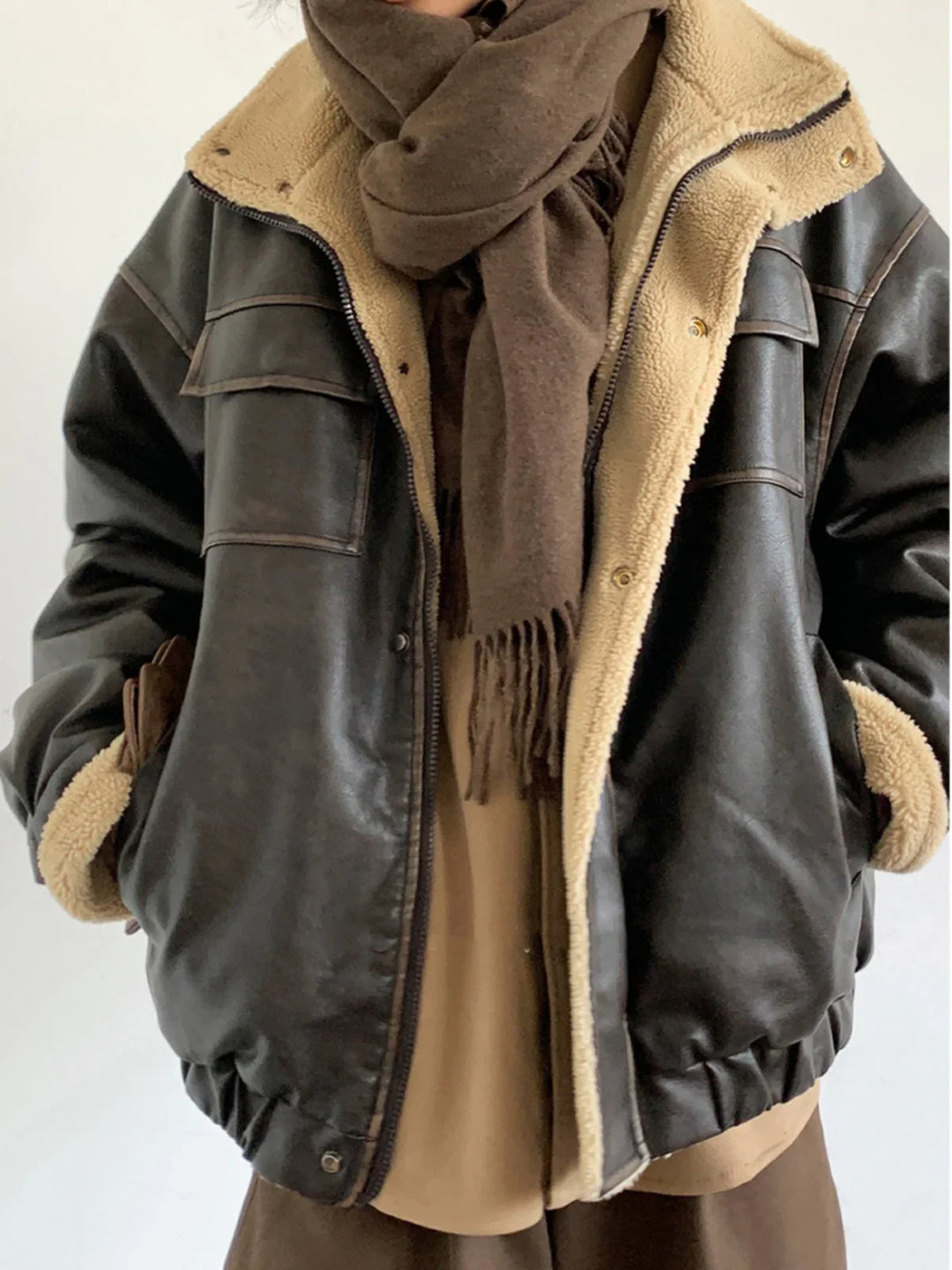 Person wearing black shearling leather jacket with beige lining and dark brown scarf