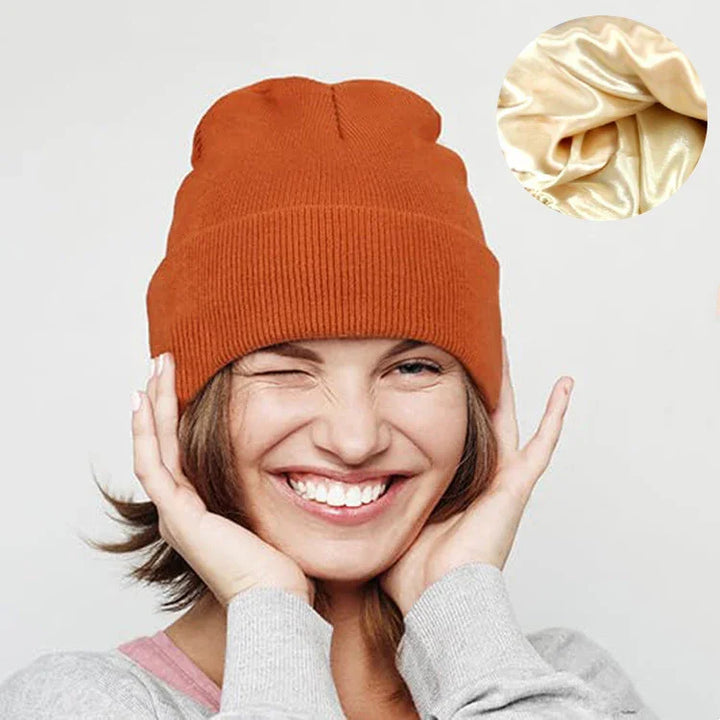 Happy woman winking wearing orange knit beanie hat and gray sweater on light background