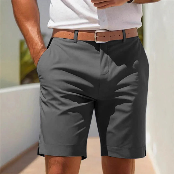 Man wearing dark gray casual shorts with a tan belt and white shirt outdoors