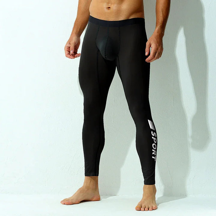 Man wearing black sports compression leggings with SPORT logo on leg against white wall