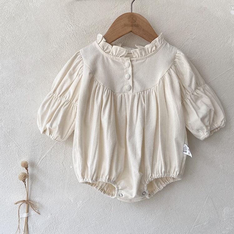 Cream-colored baby romper with ruffled collar and buttons, hanging on wooden hanger