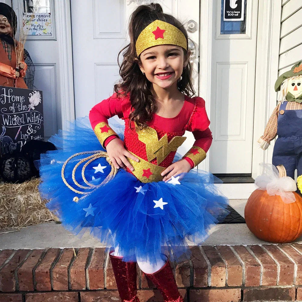 Smiling girl in Wonder Woman costume with blue tutu, gold accessories, and red boots on porch