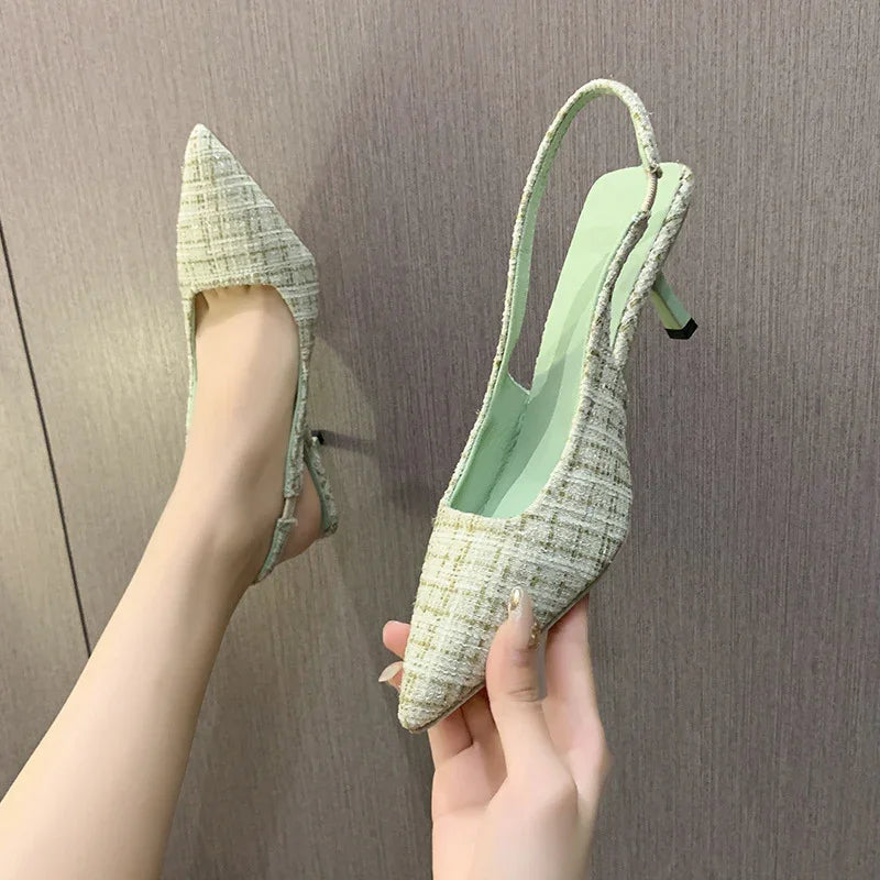 Pair of women's pointed toe slingback heels in green tweed fabric against wooden background