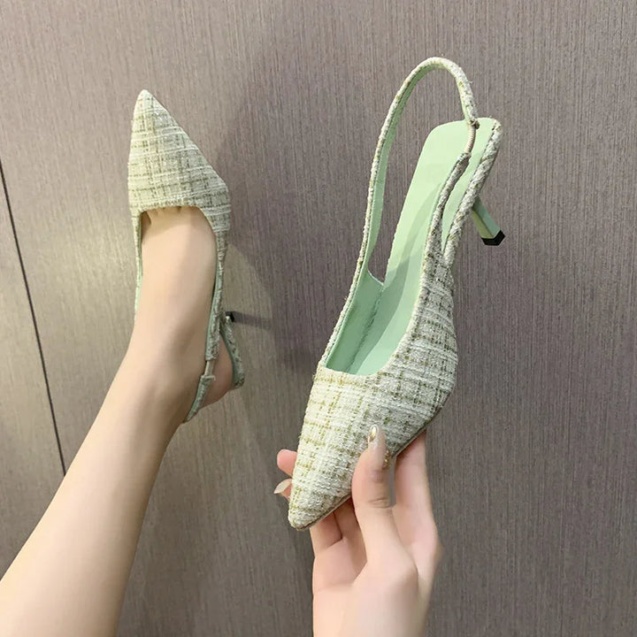 Pair of women's pointed toe slingback heels in green tweed fabric against wooden background
