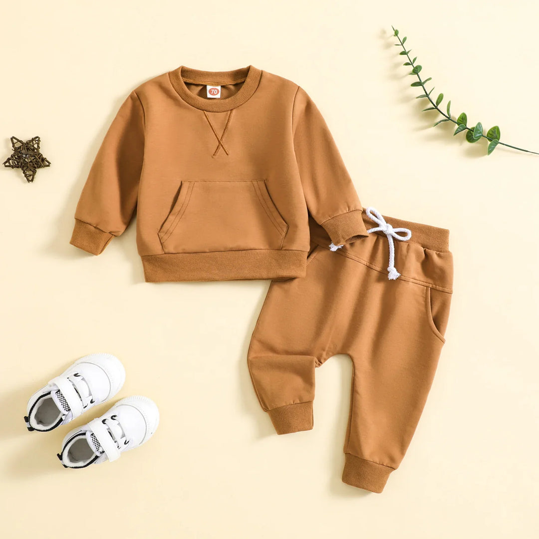 Brown toddler sweatshirt and jogger pants set with white drawstring and white baby sneakers on beige background