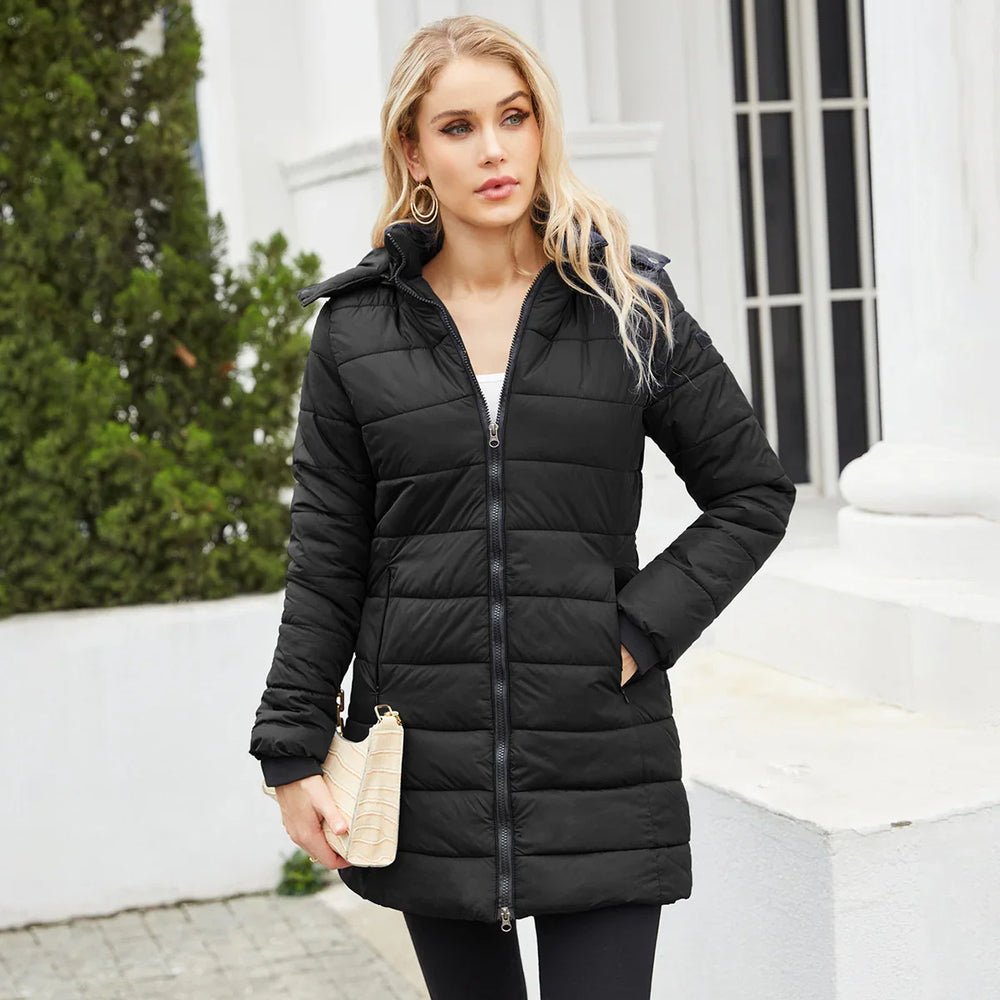 Blonde woman wearing black quilted puffer coat holding beige clutch outdoors