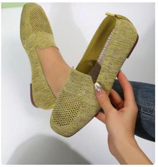 Hand holding green knitted slip-on shoes with one worn on foot against white background