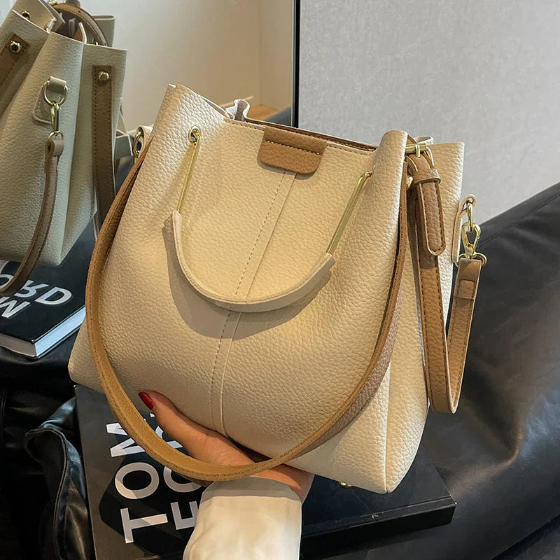 Cream leather handbag with gold hardware and tan strap held by hand near mirror and books