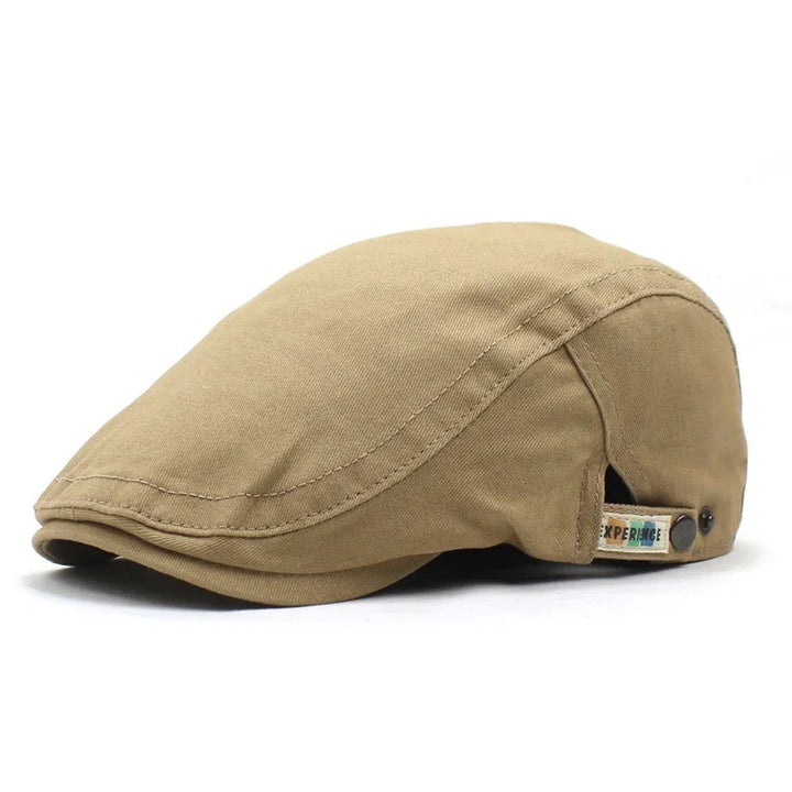 Beige flat cap with button detail and small fabric tag on side, isolated on white background