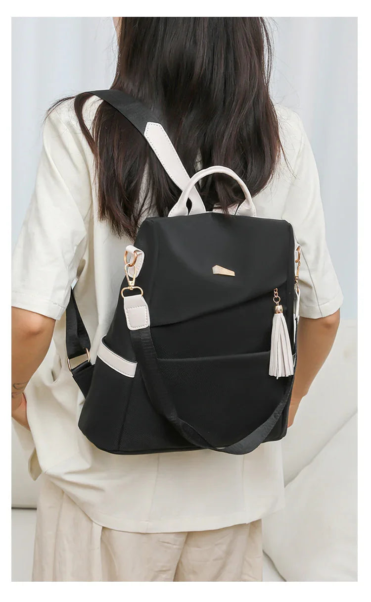 Black backpack with white handle and tassel worn by person in cream shirt and pants