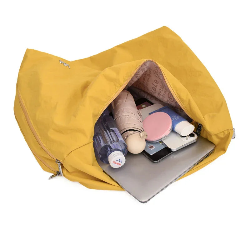 Open yellow travel tote bag with water bottle, folded umbrella, cosmetics, smartphone, and laptop inside