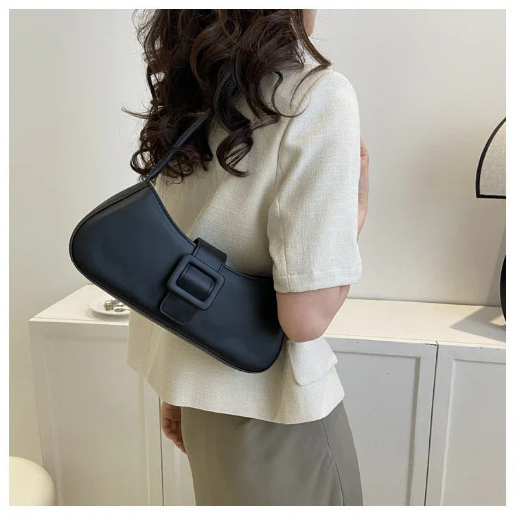 Woman wearing beige short-sleeve top and skirt, carrying black leather shoulder bag with buckle