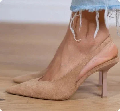 Close-up of nude beige suede pointed-toe slingback heels worn with frayed hem denim jeans on wooden floor