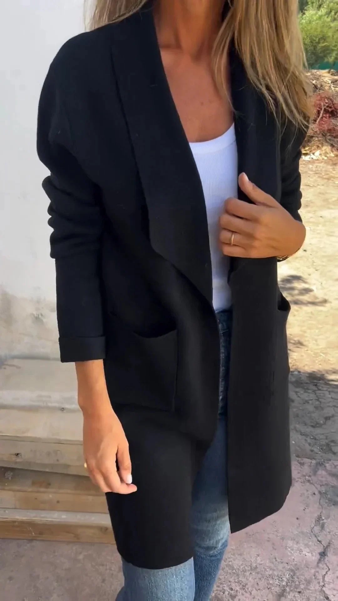 Woman wearing a black open-front cardigan over a white top and blue jeans outdoors