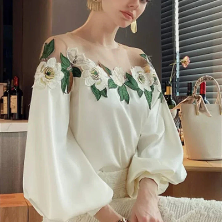 Woman wearing an off-shoulder white blouse with floral embroidery and balloon sleeves in a stylish indoor setting