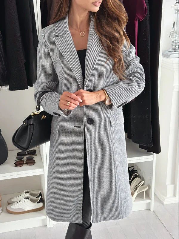 woman wearing gray herringbone long coat with black handbag in stylish closet setting