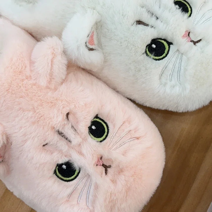 Soft plush cat face slippers in light pink and white with green eyes on wooden floor