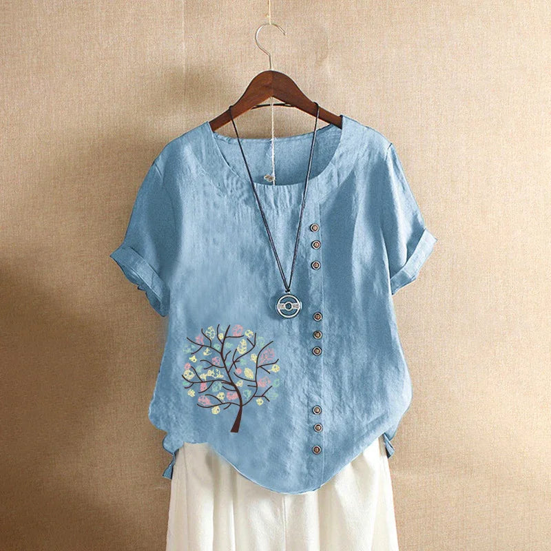 Blue short-sleeve linen blouse with decorative buttons and tree print, paired with white pants