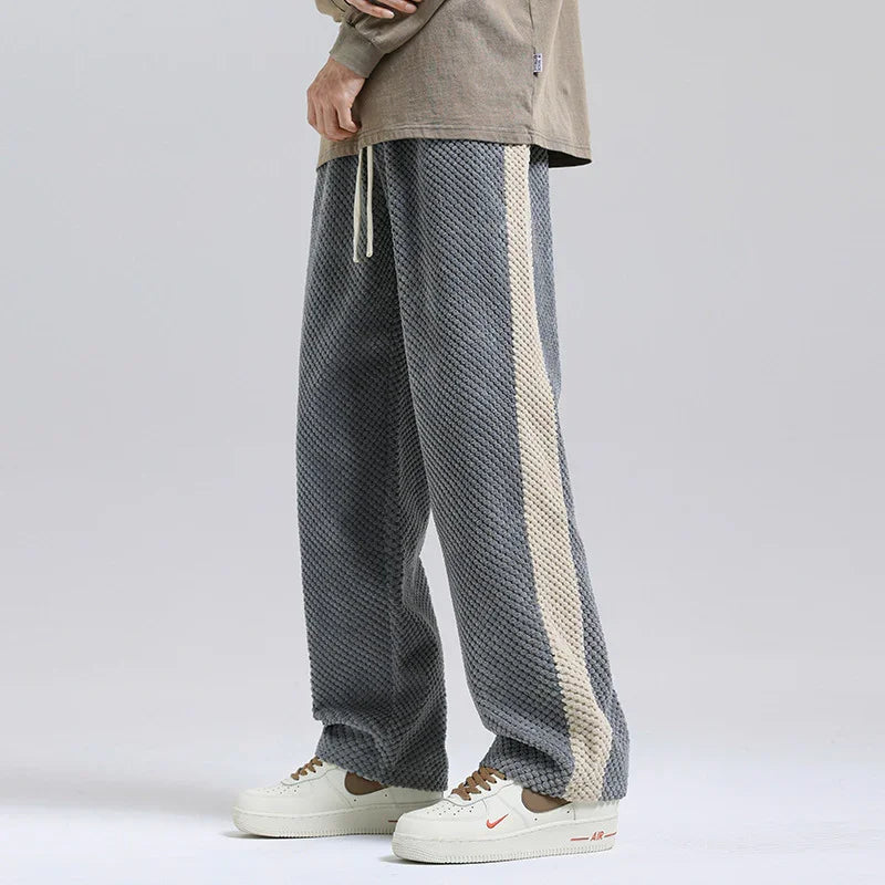 Man wearing textured gray wide-leg pants with beige side stripe and white sneakers