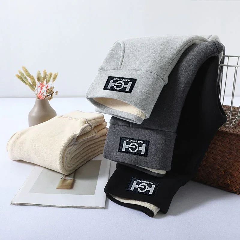 Folded warm fleece pants in beige, gray, and black with warehouse logo on a white surface near vase and basket