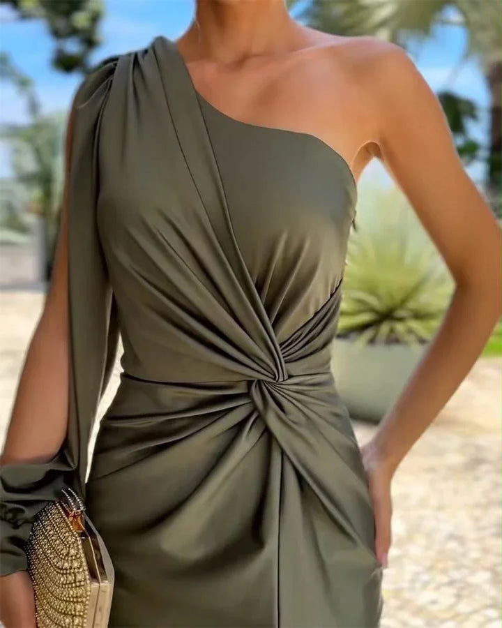Woman wearing olive green one-shoulder dress with twisted knot detail and holding embellished clutch